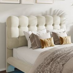 a bed with white headboard and pillows in front of three pictures on the wall