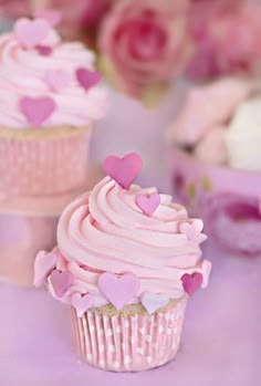 two cupcakes with pink frosting and hearts on them are sitting next to each other