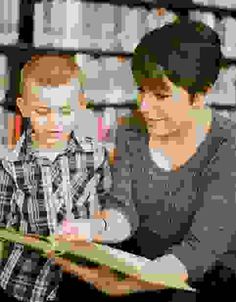 two young men sitting on a bench looking at something in front of them, one holding a book and the other reading