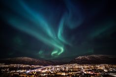 the aurora bore is in the sky above some buildings and mountains, with lights shining on them