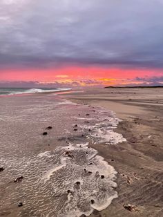 the sun is setting at the beach with waves coming in to shore and footprints on the sand