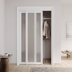 an open white closet with clothes hanging on the door and a rug in front of it