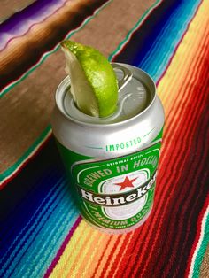 a can of beer with a lime in it sitting on a colorful table cloth next to a striped blanket