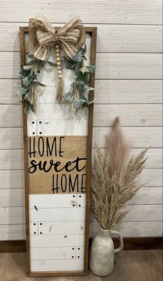 a wooden sign that says home sweet home with some plants and a vase next to it