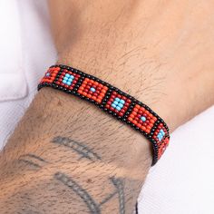 a man wearing a red and blue beaded bracelet on his arm with a tattoo