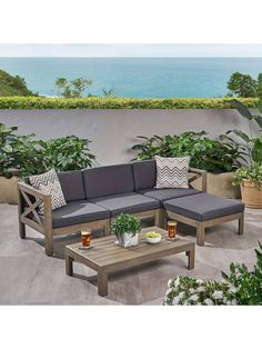 a couch and table sitting on top of a patio next to the ocean with potted plants