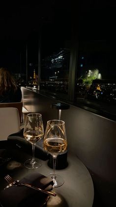 two wine glasses sitting on top of a table next to each other in front of a window