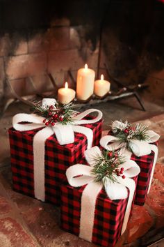 three wrapped presents sitting next to each other in front of a fireplace with lit candles