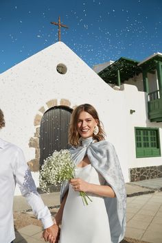 a man and woman holding hands in front of a white building with a cross on it