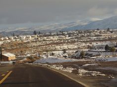 an empty street with snow on the ground and mountains in the backgrouds