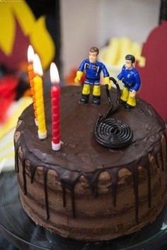 two figurines are on top of a chocolate cake with icing and candles