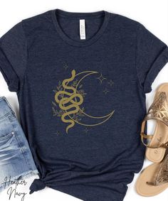 You'll love this soft, jersey tee featuring a design of a snake against a crescent moon with stars and flowers, giving off a mystical and celestial vibe. This versatile piece can be worn casually or dressed up for a semi-formal setting. Perfect for those who enjoy celestial and magical themes, suitable for everyday wear and special occasions like Halloween or Lunar New Year. The Details: *Side Seams *Ribbed Knit Collar with Seam (highly elastic and helps retain shape) *Twill Shoulder Tape (to stabilize and prevent shrinking) *Tear-away label  *Ash and Heather Prism colors - 99% Airlume combed and ring-spun cotton, 1% polyester; Heather colors - 52% cotton, 48% polyester; Athletic Heather and Black Heather - 90% cotton, 10% polyester.  *True to size *Order 1-2 sizes up for "oversized" look Crescent Moon With Stars, Celestial Snake, Snake Shirt, Gift For Daughter, Lunar New Year, Moon Stars, Prism Color, Lunar New, Nouvel An