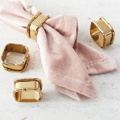 three pieces of pink cloth with gold rings on them and one piece of napkin sitting next to it