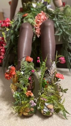 there is a doll sitting on the floor with flowers and plants around her legs,