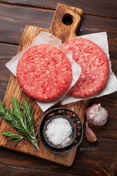 two hamburger patties sitting on top of a cutting board next to garlic and pepper