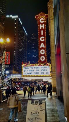 people are walking on the sidewalk in front of chicago theater at night with neon lights