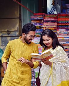 a man and woman standing next to each other in front of a book store holding an open book