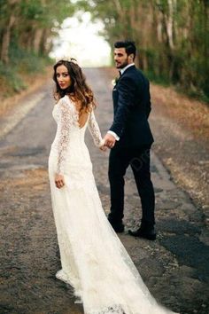 a bride and groom holding hands while standing on the road in front of some trees