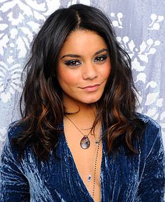 a close up of a person wearing a blue shirt and necklace with an animal print wall in the background