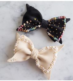 three bows with pearls on them sitting on a marble counter top, one is black and the other is white