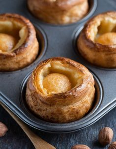 several baked pastries in a muffin tin with almonds around them on a wooden table