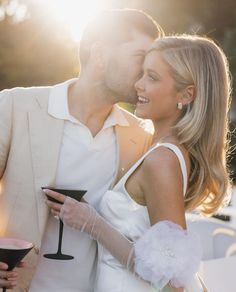 a man and woman standing next to each other holding wine glasses in front of the sun