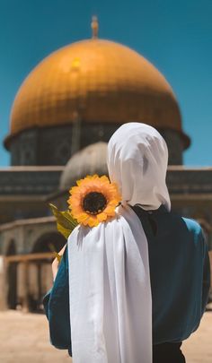 a woman with a sunflower in her hand is looking at the dome of the rock