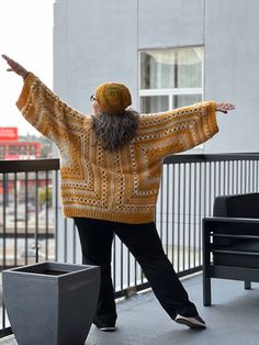 a woman in a yellow sweater and black pants is standing on a balcony with her arms outstretched