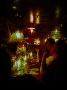 people sitting at a table in a dimly lit room with candles on the walls and lights hanging from the ceiling