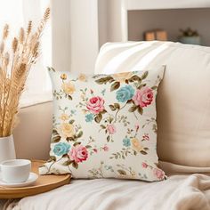 a flowered pillow sitting on top of a white couch next to a cup and saucer