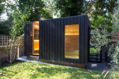 a small black building sitting on top of a lush green field next to a tree