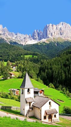 an old church sits in the middle of a green field with mountains in the background