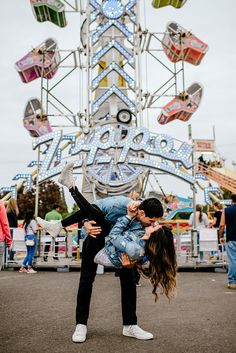 a man and woman kissing in front of a ferris wheel at an amusement park,