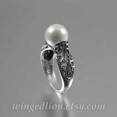 a white pearl and silver ring with filigrees on the side, sitting on a table