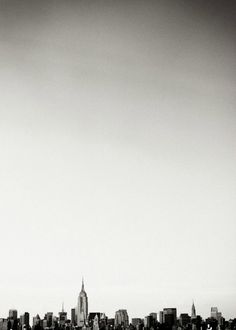 a black and white photo of a city skyline with a plane flying in the sky