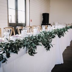 the table is set up with white linens and greenery on each place setting