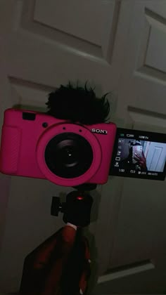 a pink camera being held up in front of a door with a person taking a photo