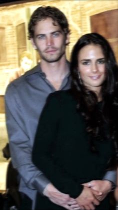 a young man and woman standing next to each other in front of a wall with lights