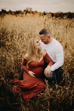 a pregnant couple cuddles in the tall grass