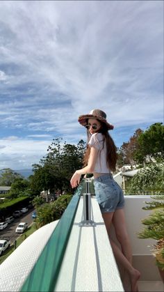 a woman standing on top of a balcony next to a green railing and wearing a hat