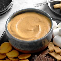 a bowl of peanut butter surrounded by crackers and marshmallows