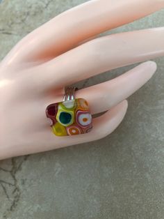 a woman's hand wearing a ring with multicolored glass beads on it