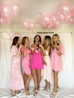 four women in pink dresses taking pictures with their cell phones at a bachelorette party