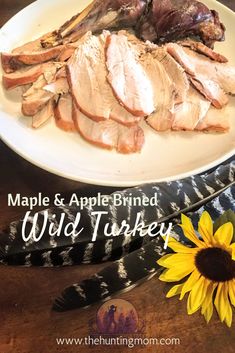 a white plate topped with meat next to a sunflower on a wooden table and the words maple & apple brined wild turkey