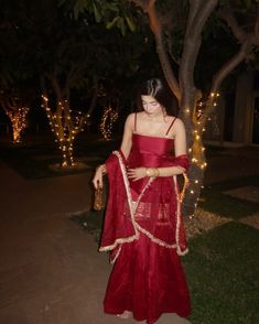 a woman in a red dress standing next to a tree with lights all around her