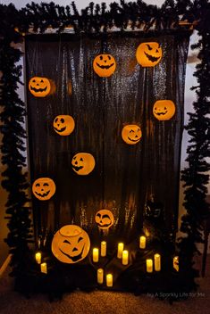 halloween decorations with pumpkins and candles in front of a black backdrop that has trees on it