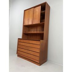 a wooden bookcase with drawers on the bottom and shelves above it, against a white wall