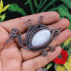 a hand holding a wire wrapped pendant with a white stone in the shape of a bird