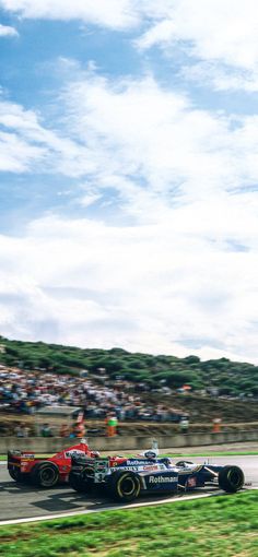 two racing cars driving on a race track with spectators in the stands watching from behind them