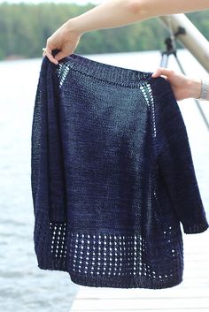 a person holding up a blue sweater on a dock by the water with trees in the background